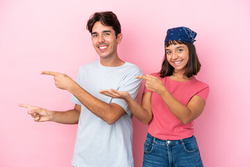 Wall Mural - Young couple isolated on pink background extending hands to the side for inviting to come