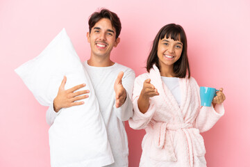 Wall Mural - Young couple in pajamas isolated on pink background shaking hands for closing a good deal