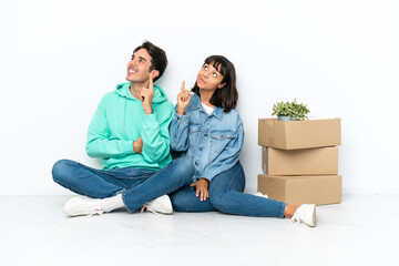 Young couple making a move while picking up a box full of things sitting on the floor isolated on white background pointing a great idea and looking up