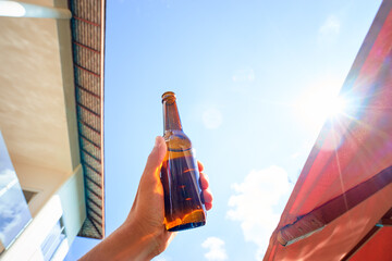 Vacation concept. Male hand holding bottle of beer against sunny sky.