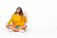 Young Woman Sitting On The Floor Isolated On White Background Saluting With Hand With Happy Expression
