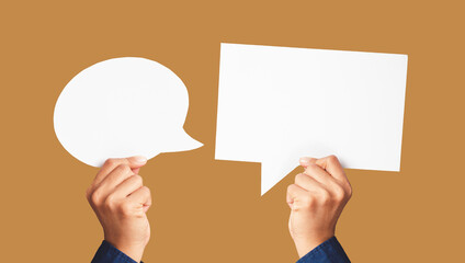 Close-up of hands holding white speech bubbles against a light brown background