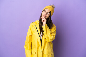 Wall Mural - Young caucasian woman wearing a rainproof coat isolated on purple background and looking up