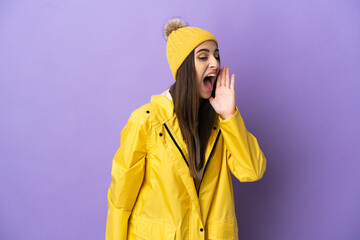 Wall Mural - Young caucasian woman wearing a rainproof coat isolated on purple background shouting with mouth wide open to the side