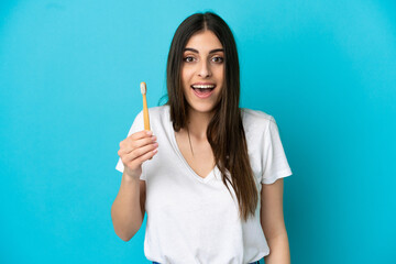 Young caucasian woman brushing teeth isolated on blue background with surprise and shocked facial expression