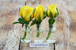 Congratulations card with three yellow roses on miniature glass bottles on wooden surface

