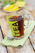 Black tea in transparent glass on checkered cloth with slices of fresh ginger, lemon and mint in the background
