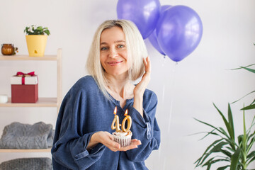 Portrait of happy middle aged woman holding birthday cake with lit candles