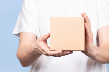 Wall Mural - Female hands holding brown rectangular cardboard box on light blue background. Mockup parcel box. Packaging, shopping, delivery concept