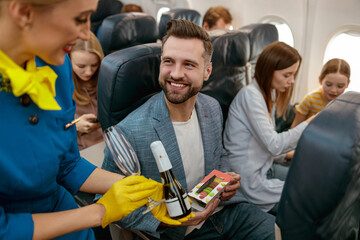 Wall Mural - Stewardess giving champagne to man in passenger airplane