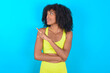 © Jihan - Portrait of young woman with afro hairstyle in sportswear against blue background posing on camera with tricky look, presenting product with index finger. Advertisement concept.