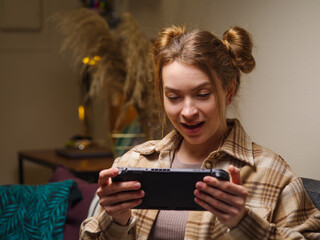 Wall Mural - Surprised girl gamer plays video games on a portable game console in the room. Virtual reality, cyberspace, mobile games, youth culture, entertainment, recreation, game strategy.