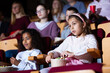 Portrait of tween girl with aframerican friend sitting in movie theater with popcorn and watching interesting film