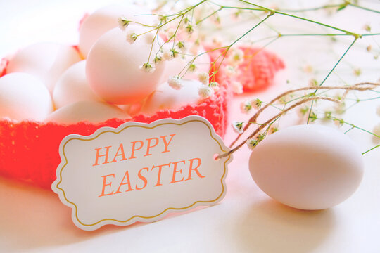Spring Easter  still life. Chicken white eggs in crochet basket with spring flowers on white background. Spring Easter card. Happy Easter text on greeting card