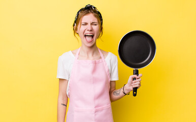 red head pretty woman shouting aggressively, looking very angry. fry pan and housewife concept