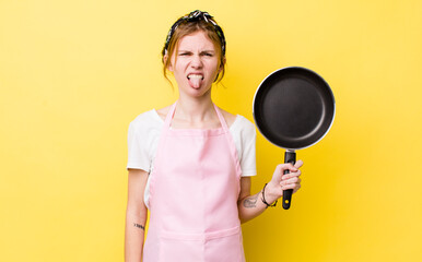 Wall Mural - red head pretty woman feeling disgusted and irritated and tongue out. fry pan and housewife concept