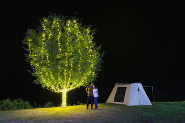 Wall Mural - couple under a tree adorn lights beside tent camping at night. there are beautiful stars in the sky.