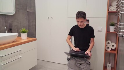 Relaxed man working online with laptop from toilet at home. Guy with a laptop on the toilet. 4k