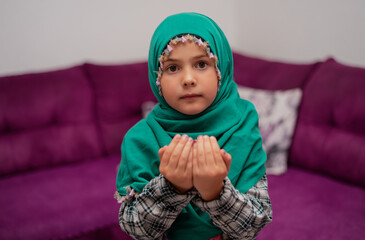 Wall Mural - Muslim child girl praying with hands up in the home.