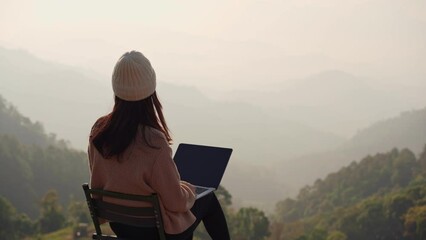 Wall Mural - Young woman freelancer traveler working online using laptop and enjoying the beautiful nature landscape with mountain view at sunrise