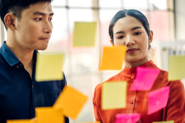 Casual creative happy two smile asian business people plan strategy analysis and brainstorm putting post it sticker note to share idea for startup project on glass board at modern office