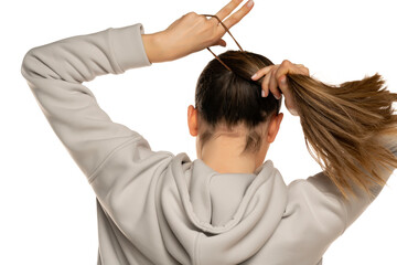 Wall Mural - a young woman in a gray tracksuit ties a pony tail to a white background in the studio