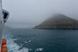 Sharp and steep rocks and cliffs of Faroese coast of Faroe Islands with mountains, waterfalls and tide in magic mystical foggy day with low hanging clouds