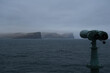 Passenger ferry Norröna Norroena passing sharp and steep rocks and cliffs of Faroese coast of Faroe Islands with mountains, waterfalls and tide in magic mystical foggy day with low hanging clouds