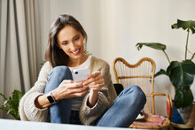 Smiling Woman Text Messaging Through Smart Phone Sitting At Home