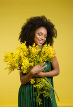 Smiling Young Woman Holding Bunch Of Mimosa Flowers Against Yellow Background