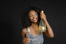 Smiling Young Woman Holding Champagne Bottle And Flute Against Black Background