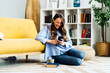 © Westend61 - Happy woman using smart phone sitting on carpet by sofa at home
