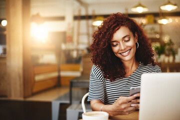 Wall Mural - Someone just sent me another compliment about my blog. Shot of an attractive young woman using a cellphone and laptop in a cafe.