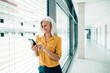 © Westend61 - Smiling businesswoman text messaging through mobile phone standing by window in office