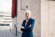 © Westend61 - Smiling business person standing with arms crossed outside office building
