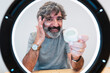 © Westend61 - Smiling senior man applying moisturizer on face seen through ring light at home