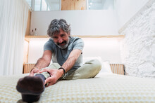 Senior Man Doing Stretching Leg Exercise On Bed At Home