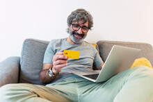 Happy Man Using Credit Card For Paying Financial Bills At Home