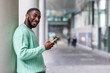 © Westend61 - Smiling man holding mobile phone standing by wall