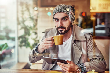 Poster - Coffee and free wifi are two of my favorite things. Portrait of handsome young man drinking a coffee and using a digital tablet while sitting at a counter in a cafe.