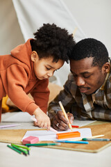 Vertical portrait of loving father and son drawing together on floor in kids room and enjoying fatherhood