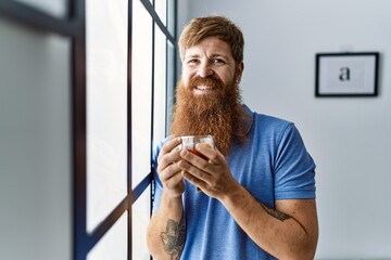 Poster - Young irish man drinking tea standing by the window at home.