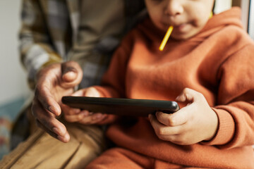 Wall Mural - Close up of black father and little boy using smartphone together and watching cartoons online, copy space