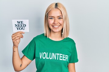 Canvas Print - Beautiful blonde woman wearing volunteer t shirt showing we need you banner looking positive and happy standing and smiling with a confident smile showing teeth