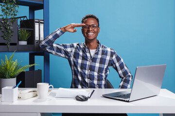 African american man doing military soldier salute while looking at camera in office workspace. Young adult person doing patriotic greeting with honor and respect for veterans servicemen.