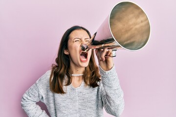 Wall Mural - Young brunette woman shouting and screaming through vintage megaphone over pink isolated background