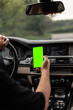 © alones - Man driver is driving and holding a smartphone with a green mockup display.