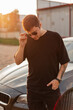 © alones - Cool fashionable man hipster in black clothes walks and puts on a stylish sunglasses