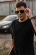 © alones - Fashionable male portrait of hipster man in black mock-up t-shirt with longboard walks on the street and wear a stylish sunglasses. Fashion, style and freedom