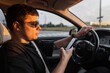© alones - Handsome Business man with sunglasses in black t-shirt is using a smartphone and driving a car at sunset